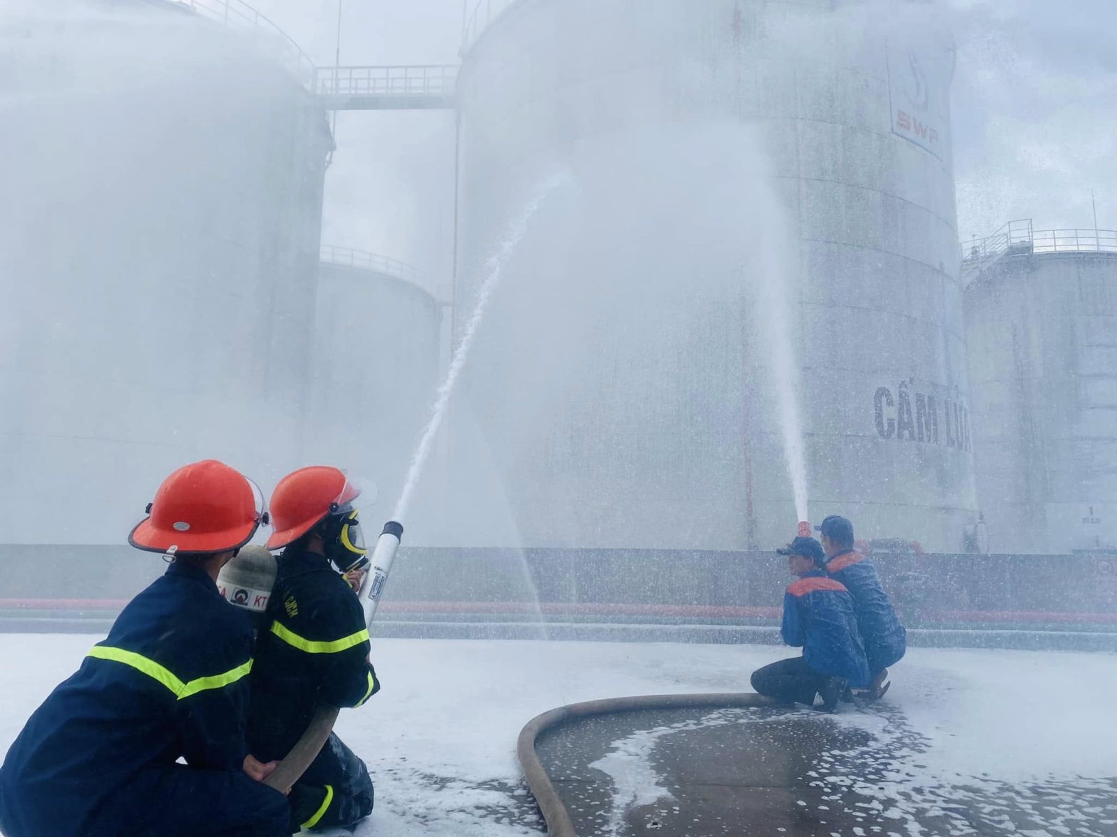 Các chiến sĩ PCCC và nhân viên kho xăng dầu phối hợp phun bọt dập lửa, thực hành thao tác cứu hỏa an toàn, chính xác.